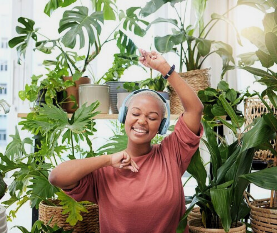 African american girl dancing while listening to music with a headset next to a huge variety of indoor plants