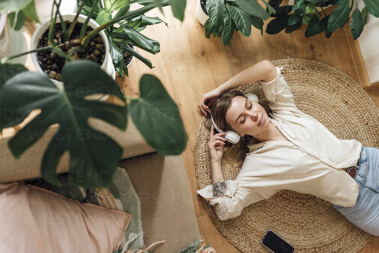 Girl relaxing listening to music on the living room floor next to her monstera.